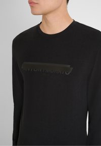 Schwarzes Langarm-T-Shirt aus Baumwolle. Es verfügt über einen mattschwarzen Grafiktext "ANTONY MORATO ITALIA" auf der Vorderseite und hat einen runden Halsausschnitt.