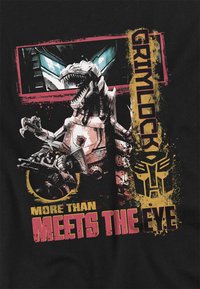 Schwarzes T-Shirt mit einem Grafikmotiv von Grimlock, einem robotischen Dinosaurier, und fettem Text "Grimlock" und "More Than Meets the Eye" in Gelb und Pink.