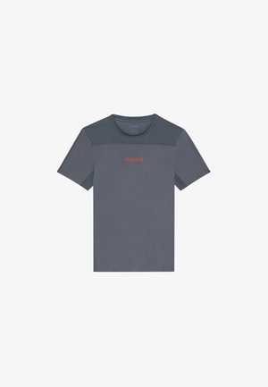 Harmaa urheilupaita, jossa on verkkomaiset yksityiskohdat, pyöreä pääntie, lyhyet hihat ja erottuva punainen "Calvin Klein" -logo rinnassa.