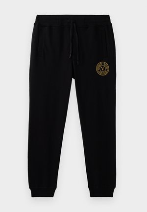 Svarte joggebukser laget av mykt stoff, med elastisk midjebånd og snor, samt sidelommer. Gullfarget rundt logo detalj på låret.