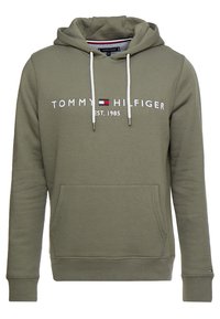 Hoodie vert olive avec poche frontale, cordons blancs et texte "Tommy Hilfiger EST. 1985" avec logo sur la poitrine.