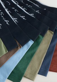 Kollektion von acht T-Shirts in verschiedenen Farben: marineblau, olivgrün, hellblau, braun, dunkelgrün, beige und rostrot. Baumwollstoff, glatte Textur.