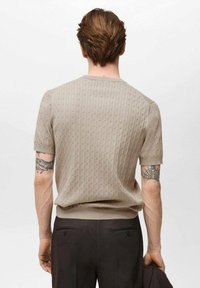 Beige Kurzarm-Strickpullover mit strukturiertem Muster, runder Ausschnitt und geripptem Saum, kombiniert mit dunklen Hosen.
