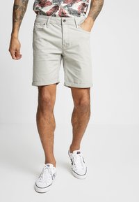Pantalones cortos de algodón gris claro con dobladillo doblado, diseño de cinco bolsillos y cierre de botón. Llevados con una camisa de estampado floral y zapatillas blancas.