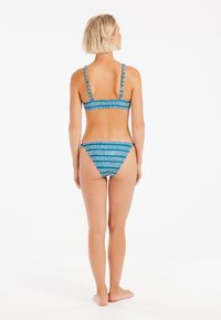 Mėlynas ir baltas raštuotas bikini, turintis bandeau tipo viršų su plonais reguliuojamais dirželiais ir atitinkančiais žemais kelnaitėmis. Sklandžios audinio tekstūros.