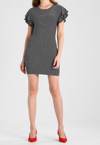 Robe à manches courtes rayée noir et blanc avec des accents à volants et une coupe ajustée, accompagnée de chaussures à talons hauts rouges.