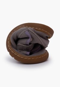 Scarpa piegata grigia realizzata in materiale morbido, con suola in gomma marrone, dettagli di cucitura e superficie testurizzata. Design leggero e compatto.