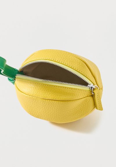 Petite pochette en cuir jaune en forme de citron, avec une fermeture éclair argentée partiellement ouverte et une sangle verte attachée.