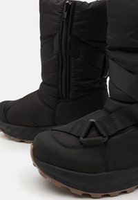 Sorte isolerte støvler med glidelås, med en teksturert overdel, gummisåle og justerbare stropper for en sikker passform.
