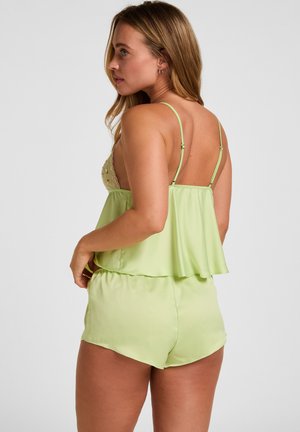 Donna in camicetta di raso verde chiaro e short abbinati vista da dietro, con spalline regolabili e dettagli in pizzo floreale.