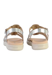 Sandalias planas con una plantilla acolchada rosa, correas metálicas plateadas y una suela exterior de un beige claro. Cuenta con correas ajustables y un diseño de apertura en la parte trasera.