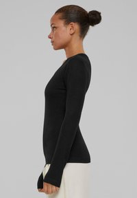 Pulover negru cu mânecă lungă, cu un design ajustat. Materialul este neted, cu tiv ondulat. Include orificii pentru degete la manșete pentru un plus de confort.