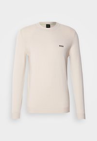 Pull crème à manches longues avec col rond, petit logo noir « BOSS » sur la poitrine gauche, présenté sur fond blanc uni.
