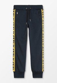 Marinblå sweatpants med elastiskt midjeband och svart dragsko; har en gul logostrip längs sidorna; två fickor med dragkedja.