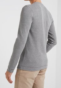Maglietta grigia a maniche lunghe con una trama a coste, scollatura rotonda e colore uniforme, vista da dietro, abbinata a pantaloni beige.