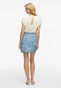 Top de algodón con mangas tipo cap sleeve, que presenta un detalle de ojal en la parte posterior. Falda de mezclilla con una base azul claro y un patrón floral blanco.