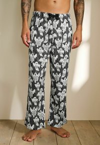 Black and white pajama pants featuring ghost patterns and text like "Boo" and "Creep it Real." Elastic waistband with drawstring detail.