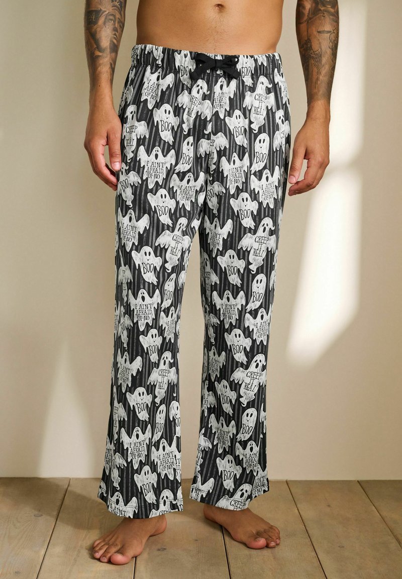 Black and white pajama pants featuring ghost patterns and text like "Boo" and "Creep it Real." Elastic waistband with drawstring detail.
