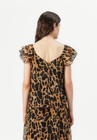 Leopardmønstret topp med gennemsigtige flæseærmer, V-rygdesign og et let, flydende stof i brune og sorte nuancer.