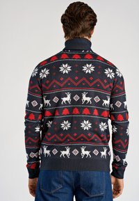 Marinblå stickad tröja med röda och vita julmönster, inklusive renar, snöflingor och träd. Hög krage och ribbade muddar.