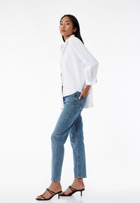 Camicia bianca a maniche puffy, jeans azzurri chiari e sandali neri con cinturino. La camicia ha un taglio morbido e i jeans hanno una vestibilità classica.