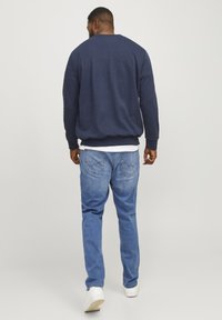 Marineblauwe sweatshirt met geribbelde manchetten, gecombineerd met lichtblauwe jeans met achterzakken en subtiele stiksels. Witte sneakers maken de look compleet.