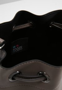 Ruskea keinonahkainen pyöreä laukku, jossa pehmeä, aaltoileva yläreuna, hopeiset metalliosat ja sisäpuolella etiketti, jossa lukee "even & ODO".