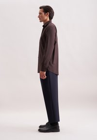 Camicia marrone a maniche lunghe con colletto a revers, abbinata a pantaloni navy e scarpe nere. Tessuto liscio; vestibilità rilassata.