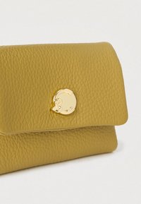 Kollane tekstuuriga nahast käekott kuldse ümmarguse kinnitusega, millel on klapi disain ja pehmed servad kompaktse silueti jaoks.