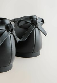 Juodos odos batai su apvalia nosimi ir žemu kulnu. Pasižymi lygiu paviršiumi ir dekoratyvinėmis kaspinėliais gale. Paprastas, klasikinis dizainas.