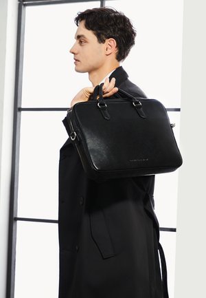 Attache in pelle nera con doppio manico superiore, forma rettangolare, texture liscia e un sottile logo sul fronte. Chiusura a zip.