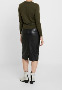 Maglione lavorato a maglia verde oliva con maniche lunghe abbinato a una gonna di pelle nera a lunghezza ginocchio con uno spacco sul retro. Stivaletti alla caviglia con motivo a serpente bianco.
