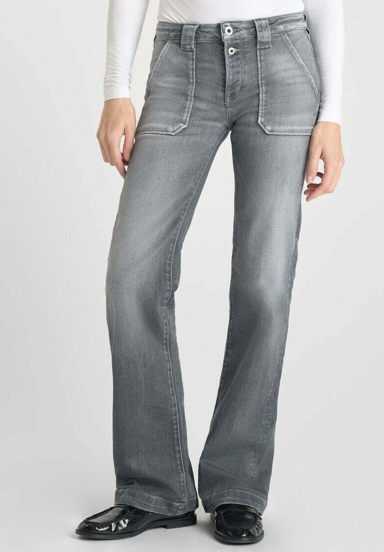 Jean évasé gris avec poches avant, double bouton à la taille et une texture denim lisse. Porté avec des chaussures noires en vernis.