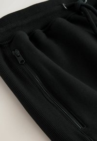 Schwarze Sweatpants mit einem strukturierten elastischen Bund, ausgestattet mit einer Taschenreißverschluss an der Seite und einem weichen Stoff-Finish.