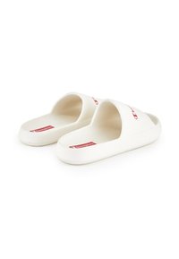 Hvide slip-on sandaler lavet af blødt plastik. Har en bred rem med en rød logo detalje. Glat tekstur og rund form.