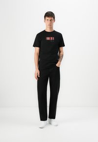 Zwarte katoenen t-shirt met een grafische print met rode en witte details, gecombineerd met zwarte broek en witte sneakers.