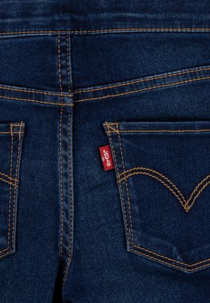 Ciemnoniebieskie tylne kieszenie dżinsów z pomarańczowym przeszyciem i małą czerwoną materiałową metką na prawej kieszeni.
