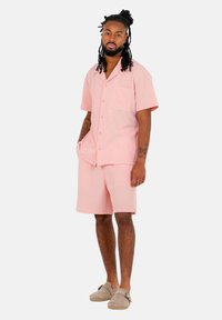Rosa kortärmad skjorta med knappar och en enda bröstficka, i par med matchande shorts. Texturerad tyg; bärs med beige slip-on skor.