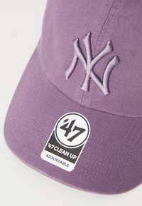 Fialová baseballová čepice s vyšitým logem NY a štítkem, který uvádí, že je nastavitelná a je součástí řady '47 CLEAN UP.