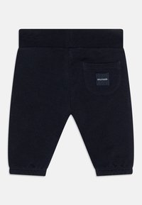 Mörkblå bomullshoodiebyxor med elastisk midja, smalnande ben och en bakficka med ett märke. Slät textur och enkel design.