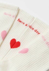 Calze al ginocchio color crema con texture a coste. Presentano la scritta rossa "have a nice day" e cuori rosa. Realizzate in morbido tessuto misto cotone.
