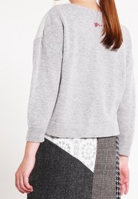 Grauer gestrickter Pullover mit lockerer Passform, rundem Ausschnitt und Dreiviertelärmeln, mit einem dekorativen bestickten Detail auf der Rückseite.