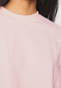 Felpa rosa chiaro con scollatura rotonda, texture morbida e maniche raglan. I dettagli delle cuciture lungo le spalle aggiungono un tocco di design sottile.