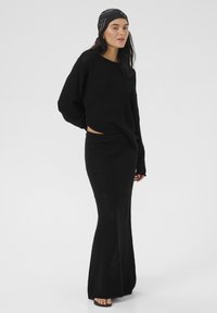 Black knit sweater and long skirt set. Loose fit with textured finish. Sweater has wide sleeves; skirt flares towards the hem. Flat sandals.