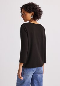 Czarny, teksturowany długi rękaw top z okrągłym dekoltem, w zestawie z jasnoniebieskimi dżinsami o luźnym kroju z tylnymi kieszeniami.