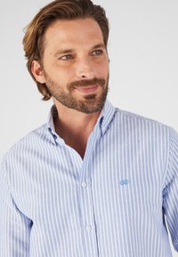 Camicia a righe blu realizzata in tessuto leggero. Caratterizzata da un colletto con bottoni, bottoni bianchi e un piccolo logo ricamato.