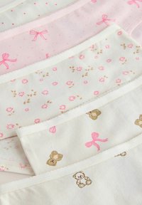 Sous-vêtements pour bébé en pastel doux avec des nœuds roses, de petites fleurs et des motifs d'oursons, disposés en chevauchement sur une surface blanche.