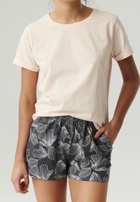 Jasnoróżowa bawełniana koszulka z podwiniętymi rękawami, zestawiona z ciemnoszarymi szortami w białe kwiaty i elastycznym pasem.