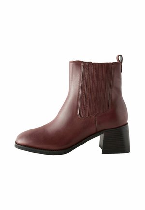 Burgundy-nahkasaappaat, joissa on paksu kanta, joustavat sivupaneelit, silmukka helpompaa pukemista varten sekä sileä, kiiltävä pinta.