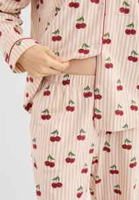 Conjunto de pijama ligero con un patrón de rayas rosas y blancas salpicado de cerezas rojas. Tejido suave, detalles con botones y cintura elástica.